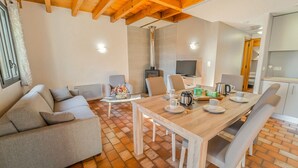 Una sala de estar acogedora con techo de madera, un sofá, una mesa de centro y una mesa de comedor lista para el desayuno.