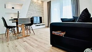 A modern living room with a black sofa, a dining table with chairs, a flat-screen TV, and a stone accent wall. - Apartment in Supetarska Draga with Seaview, Balcony, Air condition, WIFI (4325-3) (Supetarska Draga)