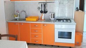 Une cuisine avec des meubles de rangement orange, une cuisinière à gaz, un évier et un petit four.