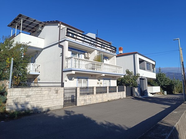 Una casa moderna a due piani con un balcone, un garage e un muro in pietra.