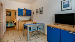 Una cucina compatta con mobili blu, un tavolo da pranzo con sedie, una TV a schermo piatto e un angolo cottura.