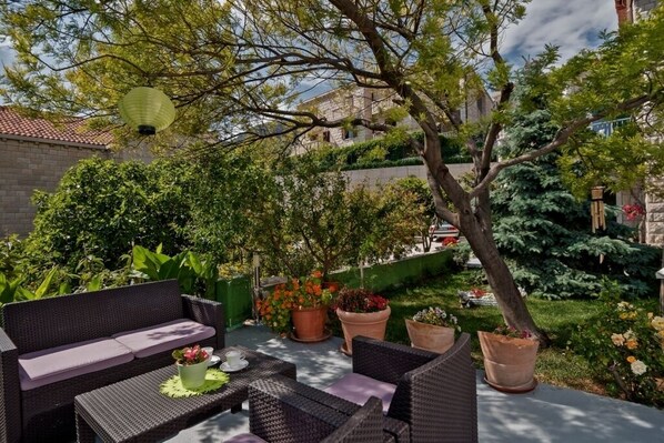 Un espace extérieur aménagé avec des meubles en osier, des plantes en pot et une vue sur un bâtiment en arrière-plan.