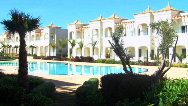A hotel with multiple white buildings featuring arched windows and a central swimming pool surrounded by greenery. - Nice apartment in Mozona Beach 4205 (Sidi Rahal)