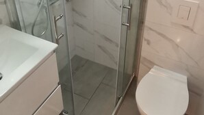 Un baño moderno con ducha de vidrio, inodoro blanco y pared cubierta de mármol.