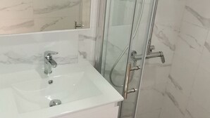 Un baño con ducha de vidrio, un lavamanos blanco y paredes con diseño de mármol.