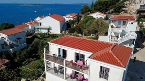 A white building with a red roof, balconies with pink chairs, and a view of the sea. - Apartment in Tribunj with Seaview, Terrace, Air condition, WIFI (4265-1) (Tribunj)