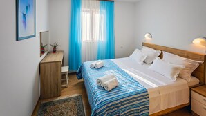 A bedroom with a bed, bedside tables, a desk, a chair, a window with blue curtains, and a framed picture on the wall. - Apartment in Rogoznica with Terrace, Air condition, WIFI, Dishwasher (3338-2) (Rogoznica)