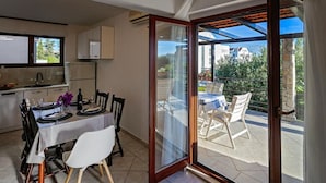 A dining area with a table set for two, a kitchen in the background, and a sliding glass door leading to an outdoor patio with chairs. - Apartment in Rogoznica with Terrace, Air condition, WIFI, Dishwasher (3338-2) (Rogoznica)