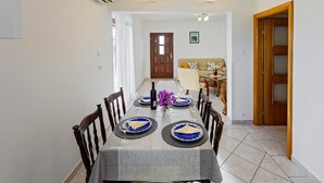 A dining area with a long table set for four, a sofa in the background, and a wooden door. - Apartment in Rogoznica with Terrace, Air condition, WIFI, Dishwasher (3338-2) (Rogoznica)