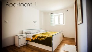 Une chambre à coucher comprenant un lit, des tables de chevet, une lampe fixée au mur et une fenêtre avec des rideaux.