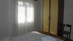 Ein Schlafzimmer mit Bett, Kleiderschrank, Stuhl und einem Fenster mit Vorhängen.