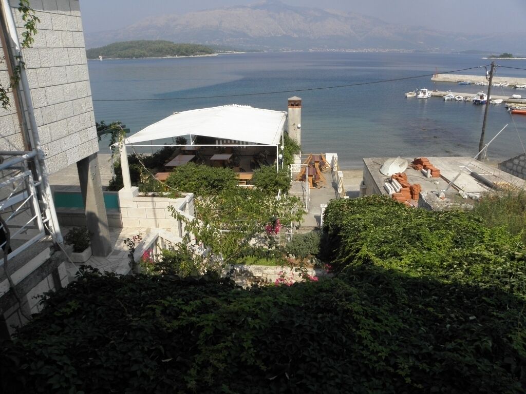 A view of a building with a terrace overlooking a body of water, with boats docked nearby.
