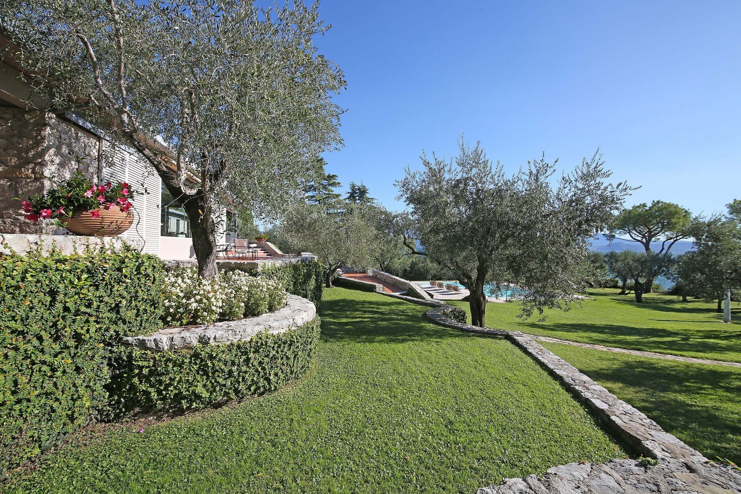 A well-maintained garden with a stone wall, a hanging flower pot, and a clear view of a building with a balcony.