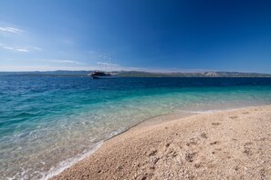 A beach with clear turquoise water and a boat in the distance. - Apartment in Bol with Seaview, Terrace, Air condition, WIFI (155-1) (Bol)