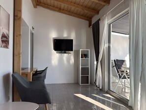 A modern room with a flat-screen TV mounted on the wall, a grey chair, a white bookshelf, and a sliding glass door leading to an outdoor area. - Apartment in Tribunj with Seaview, Terrace, Air condition, WIFI (68-2) (Tribunj)