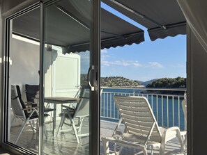 Ein Balkon mit Tisch und Stühlen, einer Glastür und Blick auf das Meer und die Hügel.