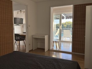 A bedroom with a bed, a desk, a chair, and a TV. There is a balcony with a chair and a table.