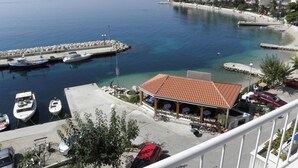 A coastal marina with boats docked, a restaurant with outdoor seating, and a view of the sea and nearby buildings.
