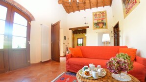 Una sala de estar con un sofá rojo, una mesita redonda con tazas y un jarrón, un radiador y una puerta que da a otra habitación.
