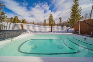 Una piscina con cubierta de madera, rodeada por una cerca metálica y suelo cubierto de nieve.