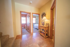A hallway with carpeted stairs, wooden doors leading to a bedroom, and a small wooden cabinet with a lamp.