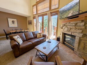 A living room with a brown leather sofa, a wooden coffee table, a stone fireplace, and a television mounted on the wall. - Gorgeous Mountain Views, Hot Tub (Keystone)
