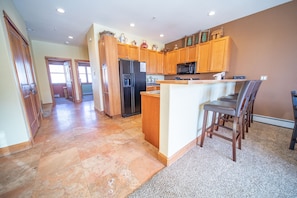 A spacious kitchen with wooden cabinets, a refrigerator, a microwave, and a bar area with chairs.