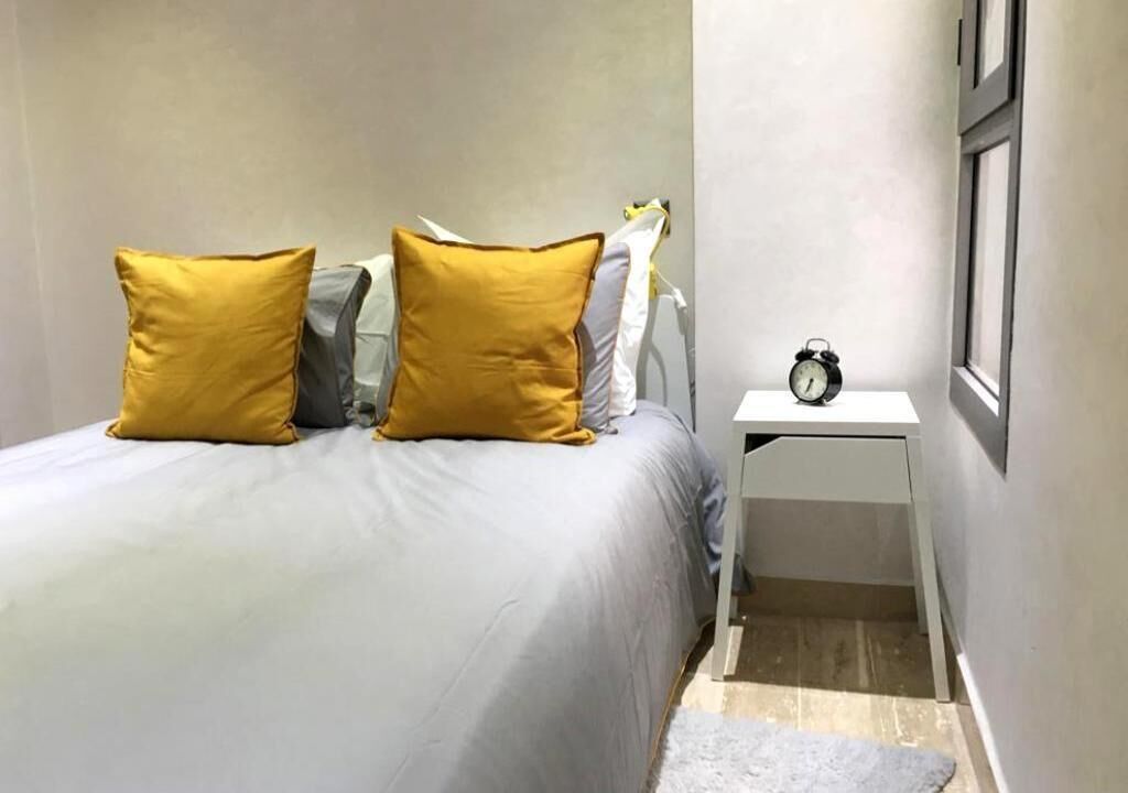 Ein Schlafzimmer mit einem Bett, zwei Kissen, einem Nachttisch mit einer Uhr und einem kleinen Teppich.