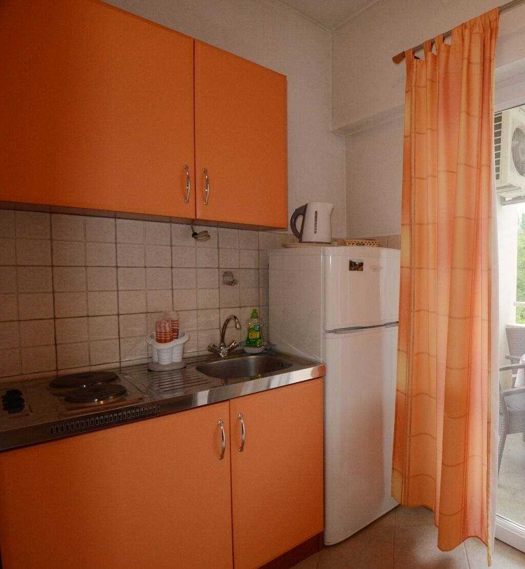 Uma cozinha com armários cor de laranja, uma geladeira branca, uma pia e uma janela com cortina.