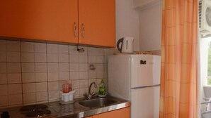 Une cuisine avec des meubles de couleur orange, un réfrigérateur blanc, un évier et une fenêtre avec un rideau.
