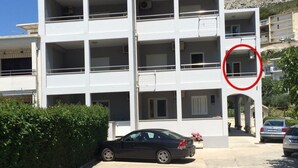 Un immeuble à plusieurs étages doté de balcons, d’un espace de stationnement et avec une montagne en arrière-plan.