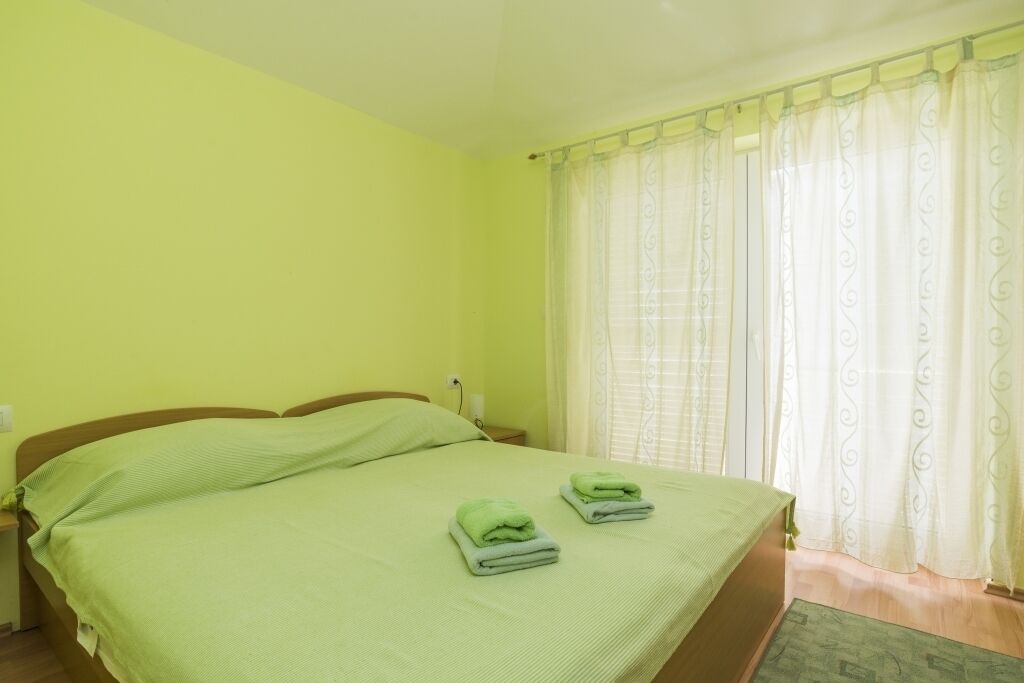 Ein Zimmer mit einem Bett, zwei gefalteten Handtüchern, einem Nachttisch und einem Fenster mit Vorhängen.