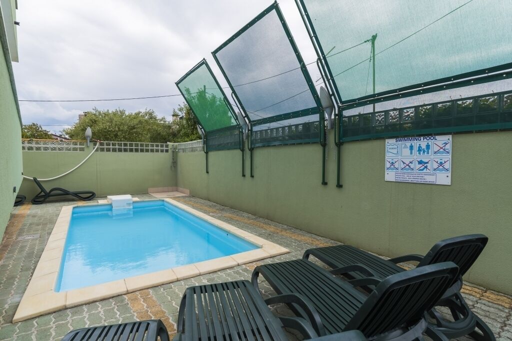 Ein Schwimmbecken mit Glasveranda, einem Schlauch und einem Schild mit den Poolregeln.