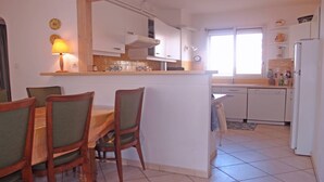 Una cocina con comedor, armarios blancos, estufa y ventana.