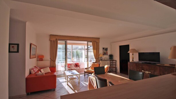 Una sala de estar con un sofá rojo, una mesa de centro y un televisor. Hay una ventana con cortinas y vistas al exterior.
