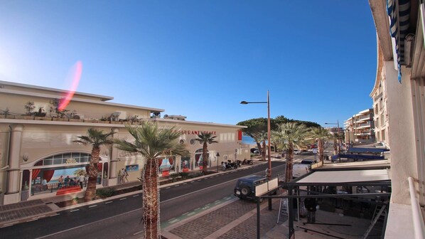 Vista de la calle con un restaurante llamado "Restaurant Place" a la izquierda, palmeras bordeando la carretera y un cielo azul despejado.