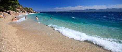 A beach with clear turquoise water, a sandy shore, and a few people enjoying the water.