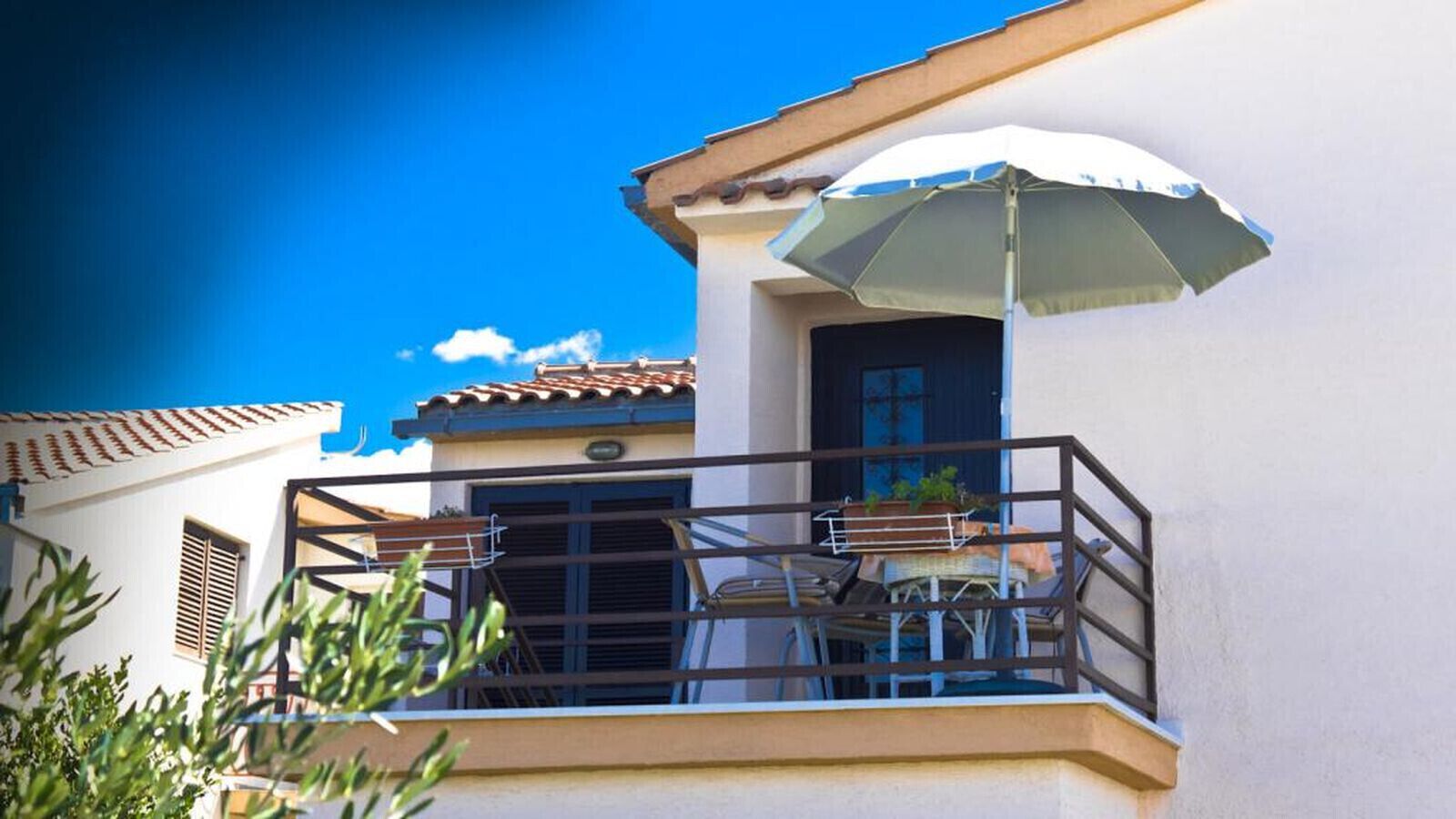 A balcony with a table and chairs, a potted plant, and a white umbrella.