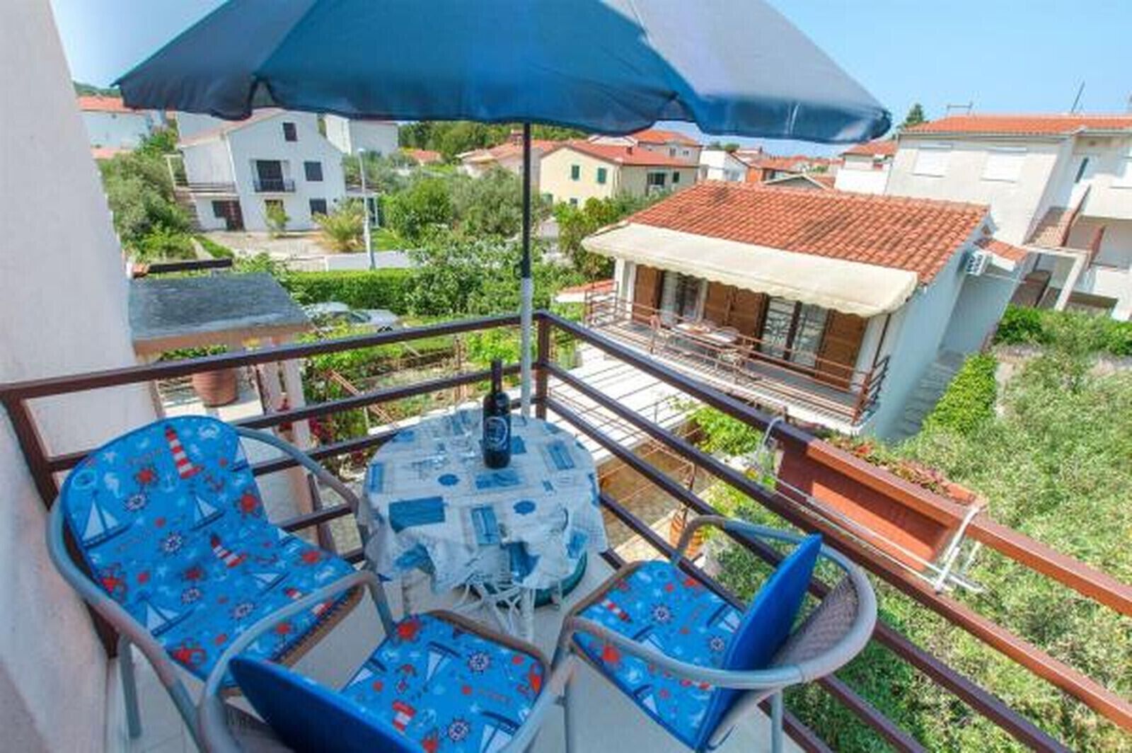 A balcony with a table and chairs, a blue umbrella, and a view of surrounding buildings.
