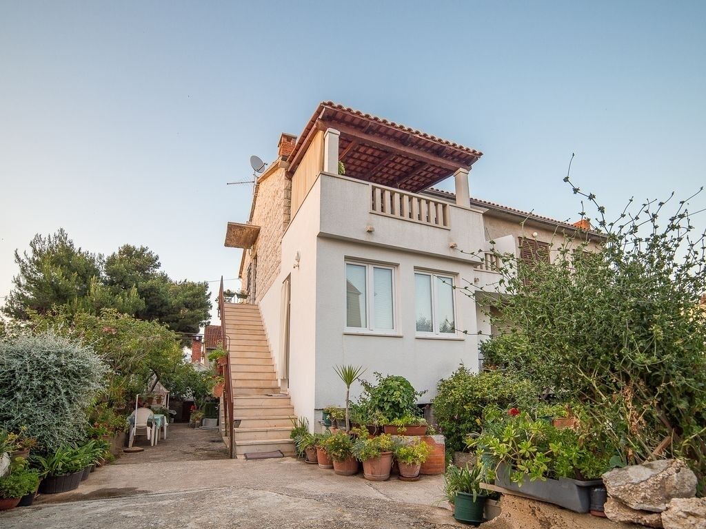Une maison à deux étages dotée d’un patio couvert, d’un escalier et de diverses plantes en pot.