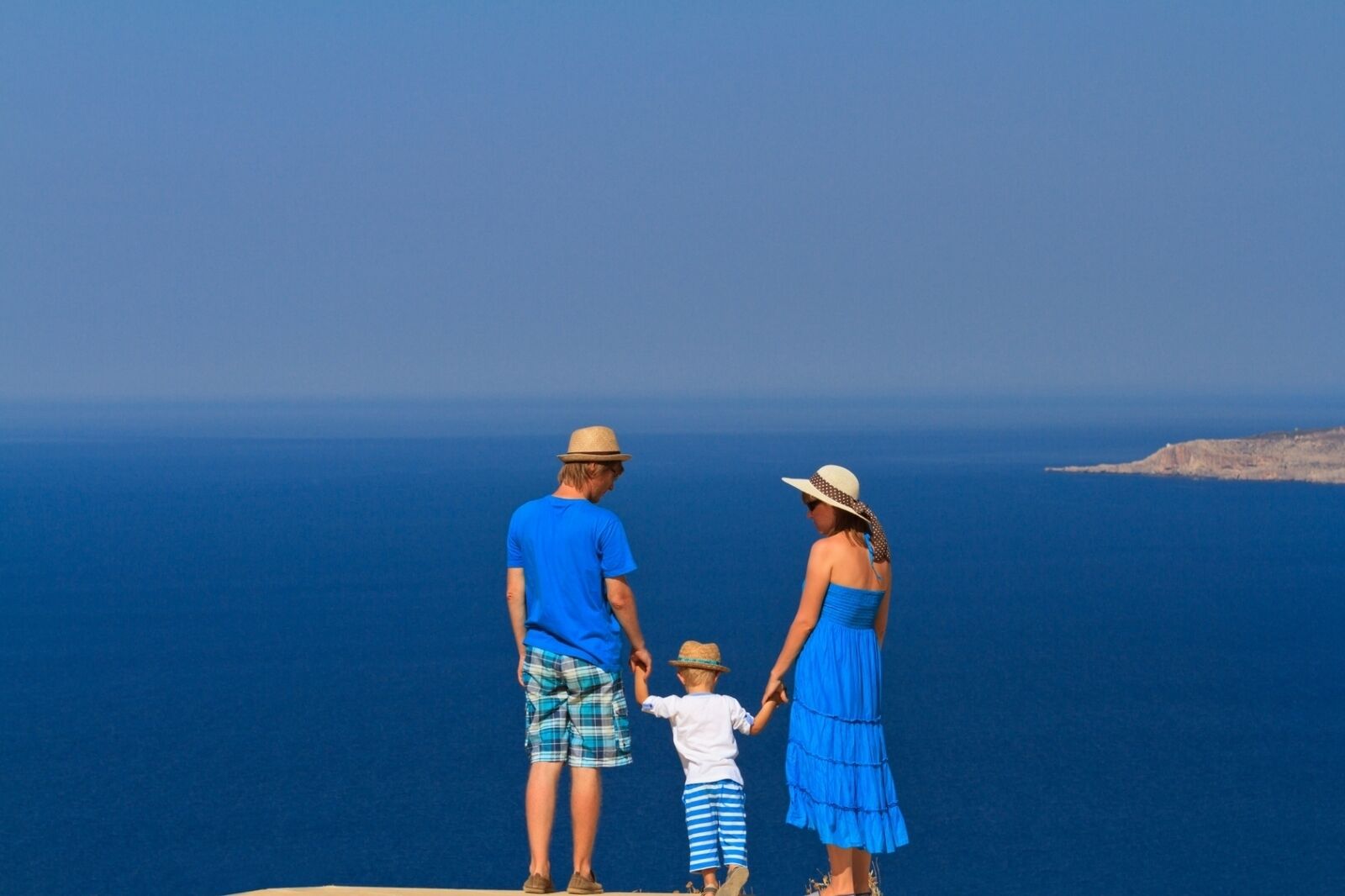 A family of three standing on a cliff overlooking a vast ocean.