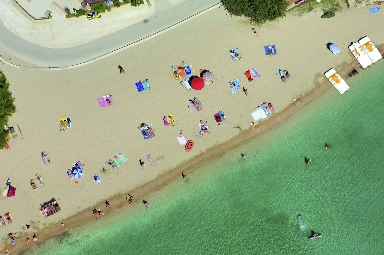 An aerial view of a beach with people, umbrellas, and beach chairs.