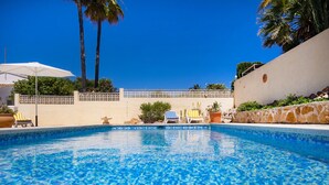 Una piscina cristallina con lettini e ombrelloni, circondata da palme e un recinto bianco.