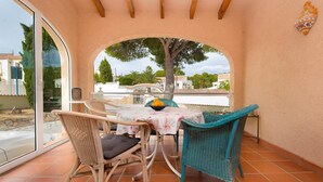 Un patio con sedie in vimini, un tavolo, una porta vetrata e vista su alberi e palazzi.