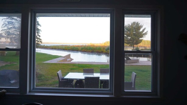 A view through a window with a sign reading 'West Twin Lake,' a grassy area, a table with chairs, and a body of water. - Firefly Cottage | West Twin Lake Getaway (Lewiston)