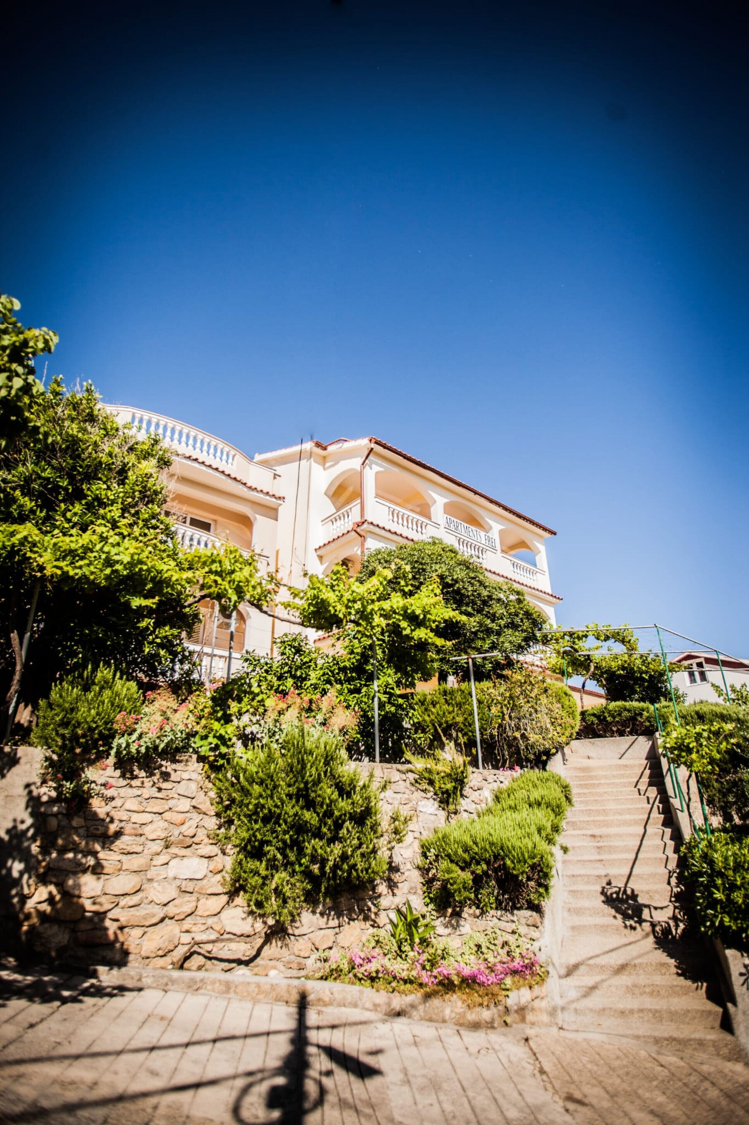 A multi-story building with balconies, surrounded by greenery and stone pathways.