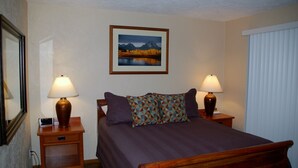 A neatly arranged bedroom with a bed, two bedside tables with lamps, a framed picture on the wall, and a window with blinds. - On the Promenade 1st floor. Spectacular Panoramic Ocean Views, Patio with grassy (Seaside)
