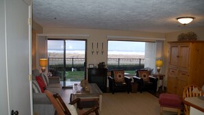 A living room with a sofa, chairs, a table, and a view of the beach through large windows. - On the Promenade 1st floor. Spectacular Panoramic Ocean Views, Patio with grassy (Seaside)