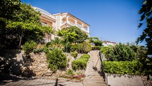 A multi-story building with a stone facade, a staircase leading to the entrance, and lush greenery surrounding the property. - Holiday Home in Lopar with Seaview, Terrace, Air condition, WIFI (186-5) (Lopar)