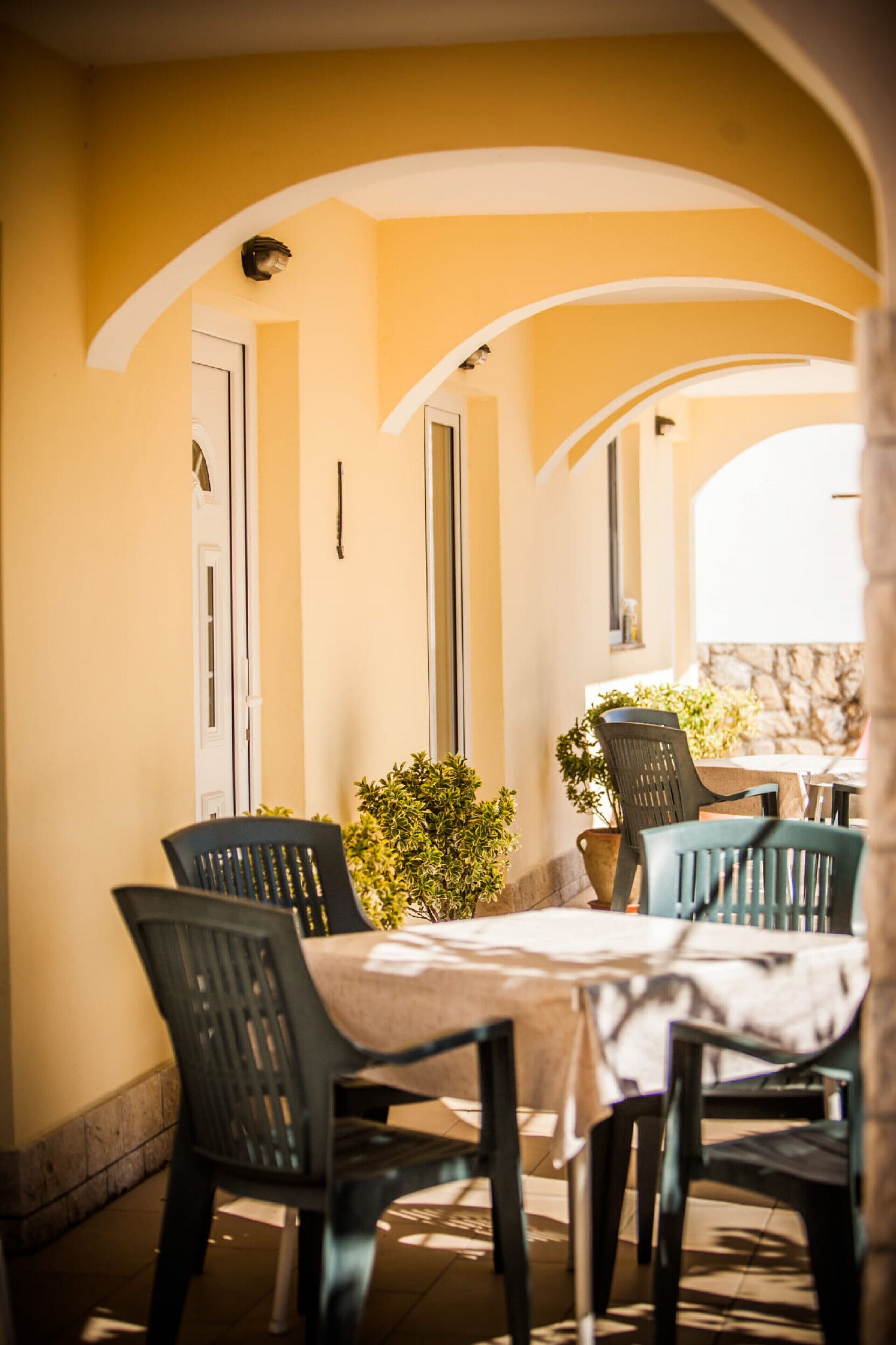 Une terrasse extérieure avec une table et des chaises, entourée d’arcades et d’une porte.